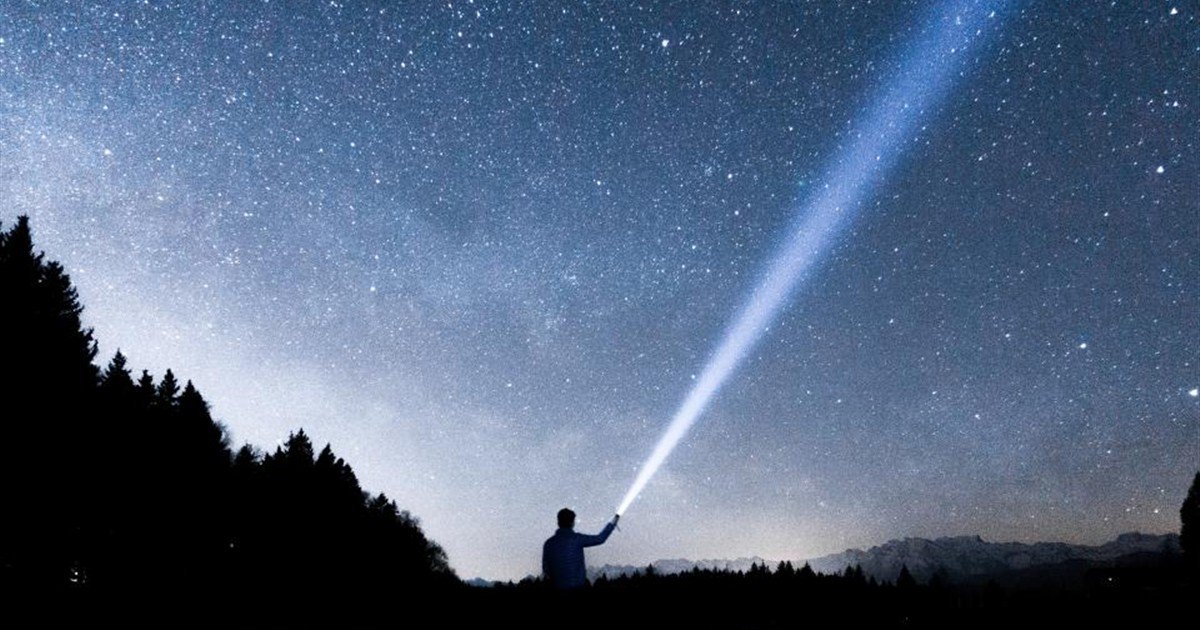 Person shining a flashlight into the dark night sky during a power outage