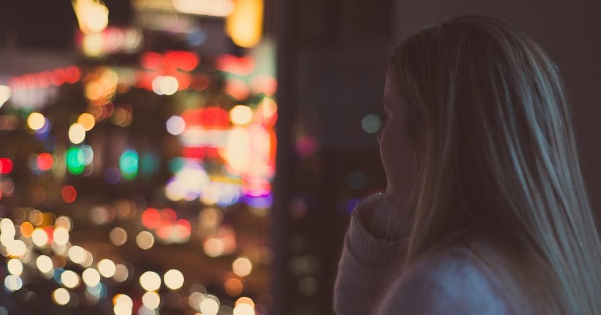 Woman looking out of a window at night over blurred city lights