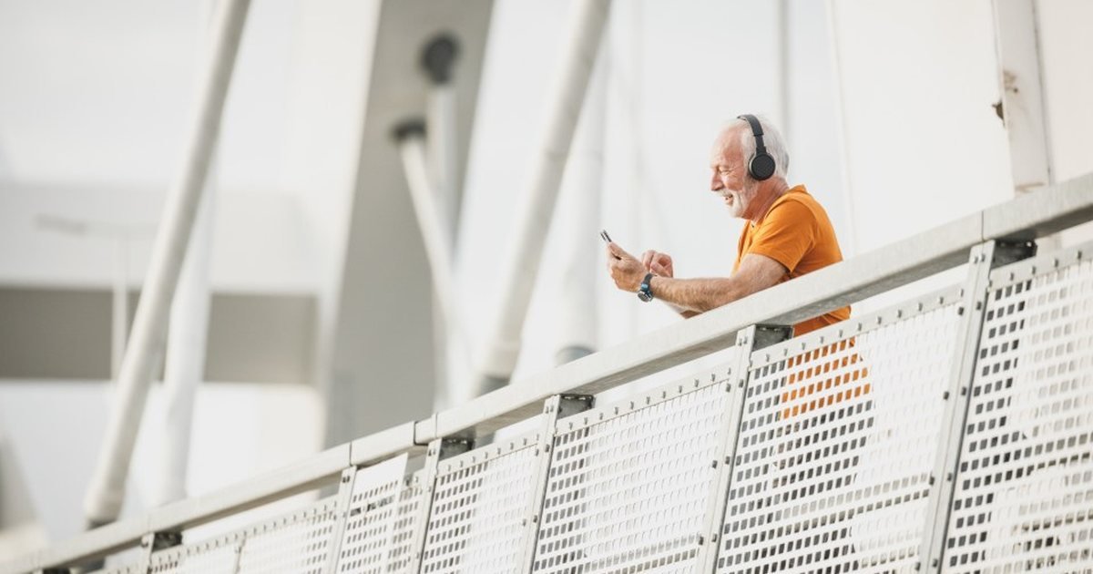 Older man in an orange shirt with headphones pausing during a walk on a footbridge