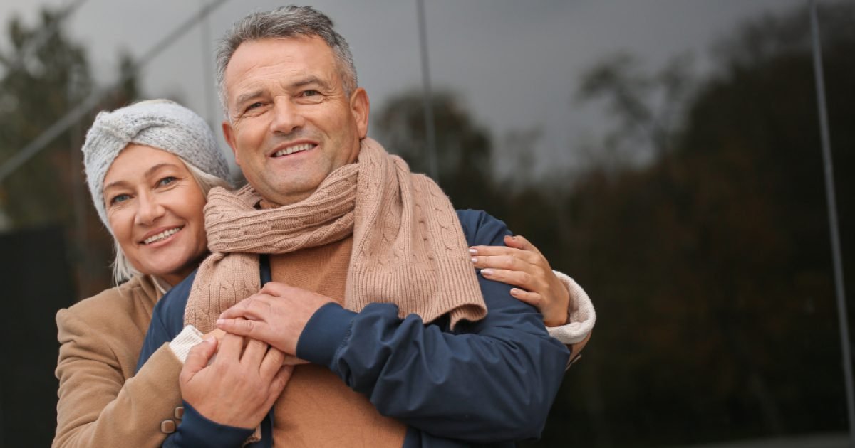 Older couple standing outdoors together in autumn coats and scarves