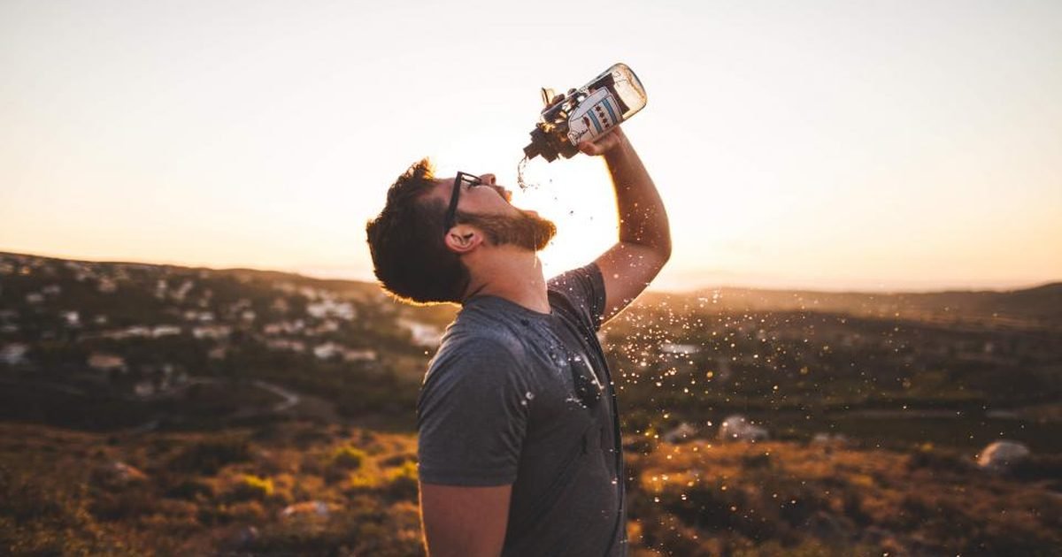 Man drinking water from a bottle outdoors at sunset