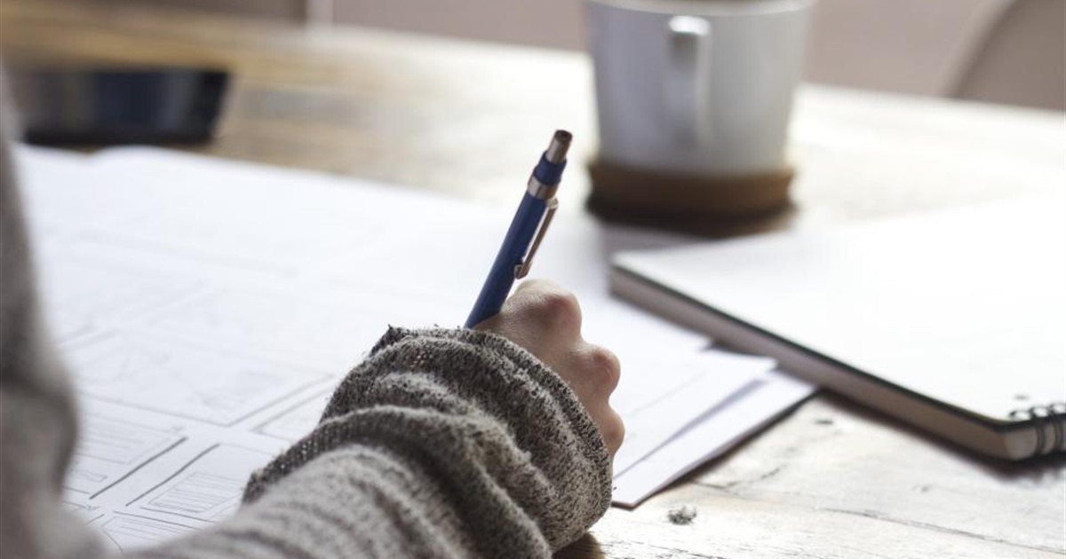 Writer drafting ideas by hand in a notebook next to a cup of coffee