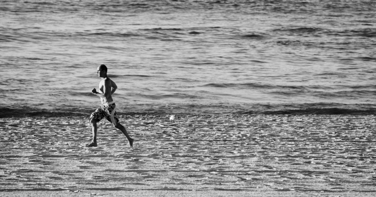 Man running along a beach at the water's edge
