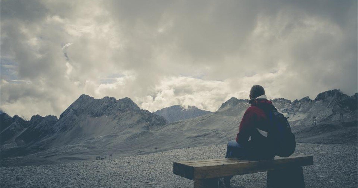 Man sitting alone on a bench facing the mountains, thinking about his next step