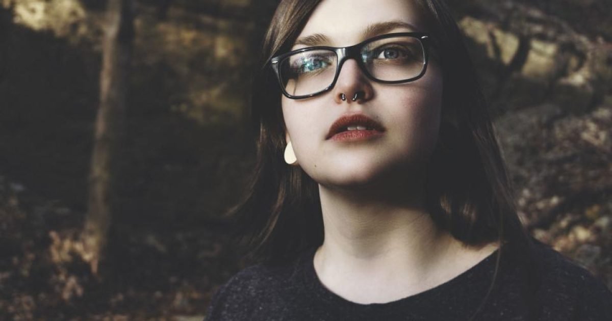 Woman wearing glasses standing outdoors in front of trees