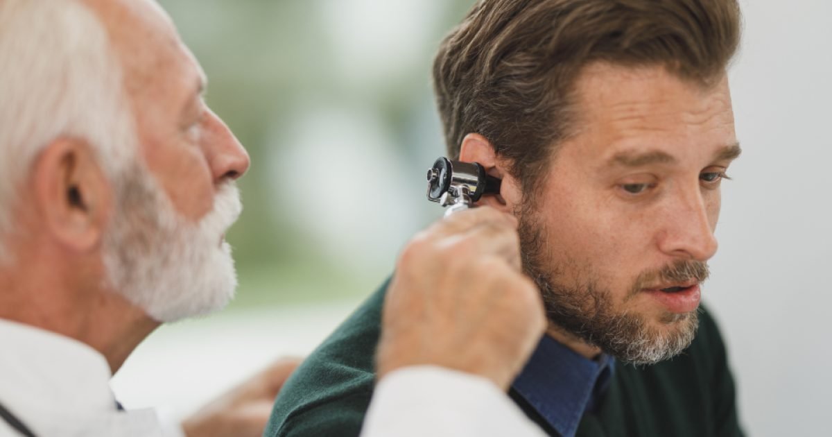 Doctor examining a middle-aged man's ear with an otoscope