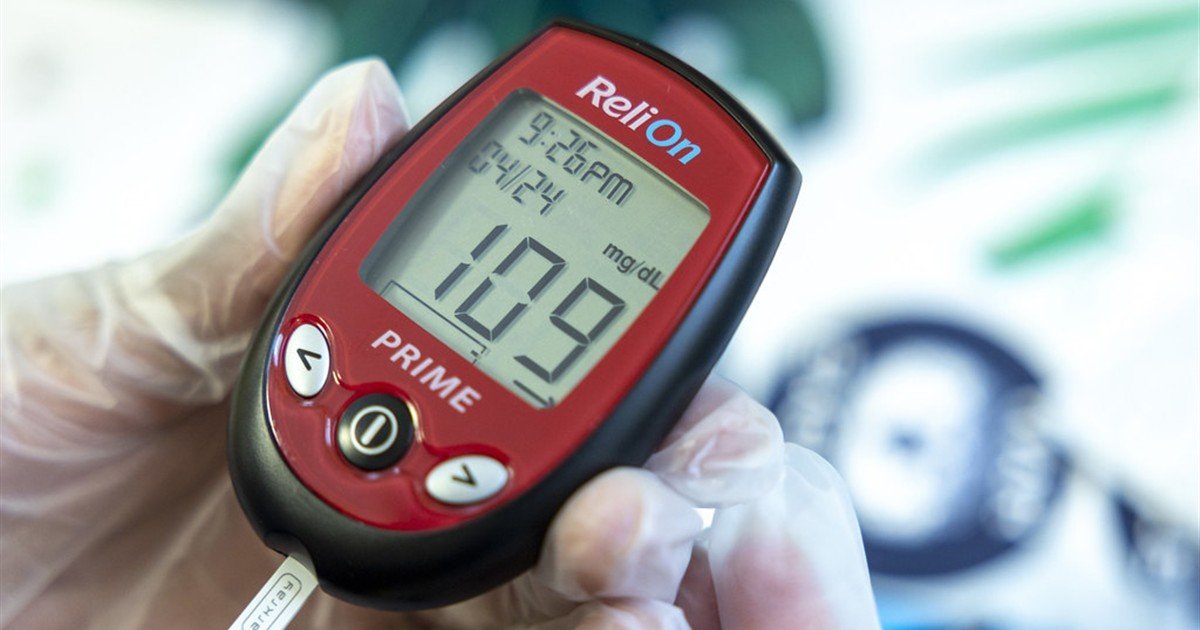 Hand holding a glucose meter showing a blood sugar reading