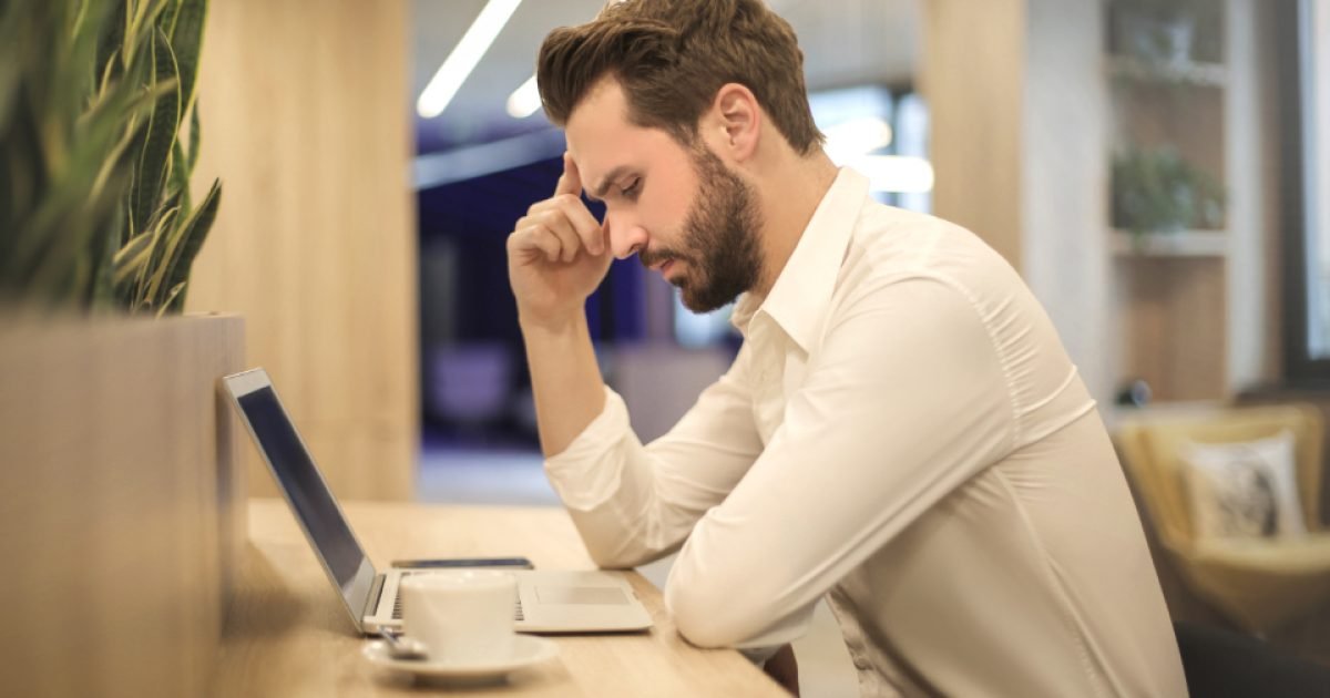 Man in a white shirt resting his head on his hand while sitting at a laptop