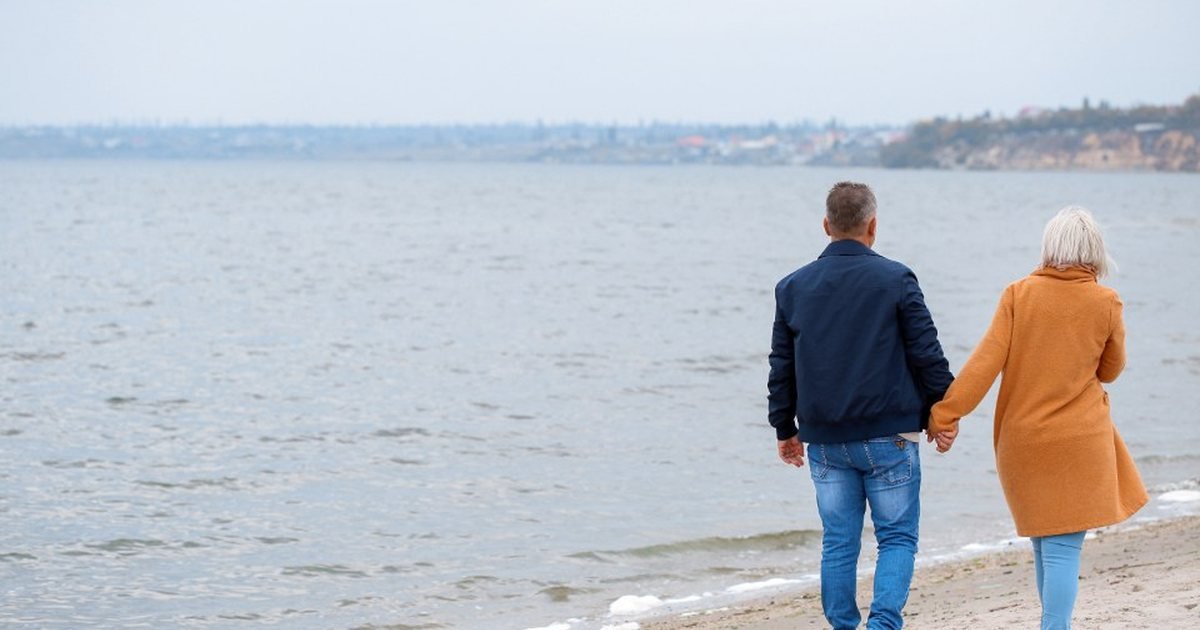 Older couple holding hands while walking along a beach shoreline