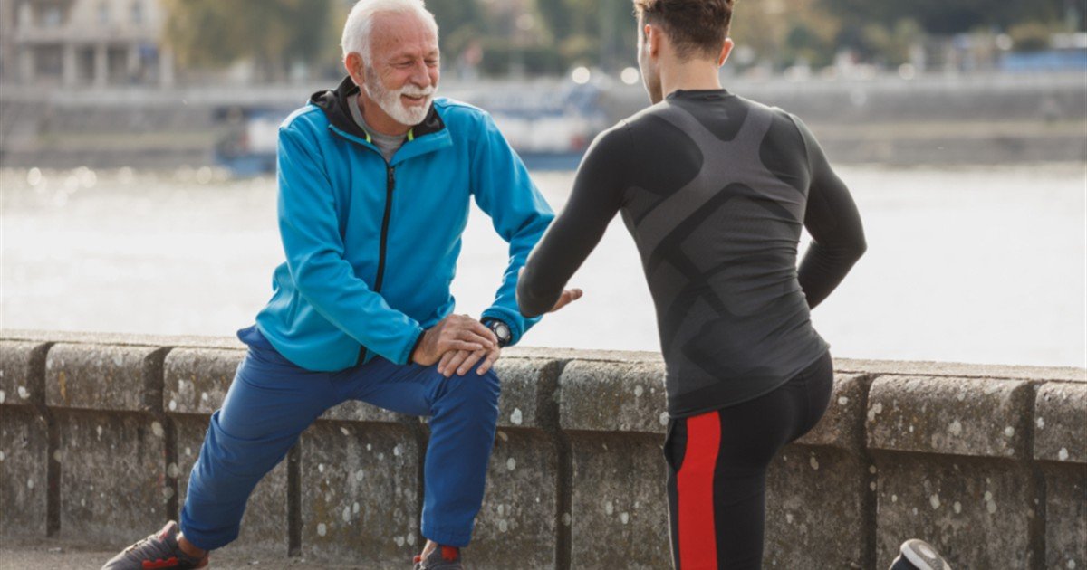 Senior man stretching outdoors with a trainer to loosen stiff morning joints