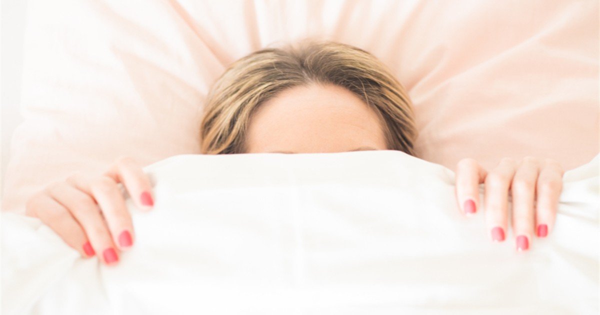 Woman lying awake in bed at night holding the duvet up to her face