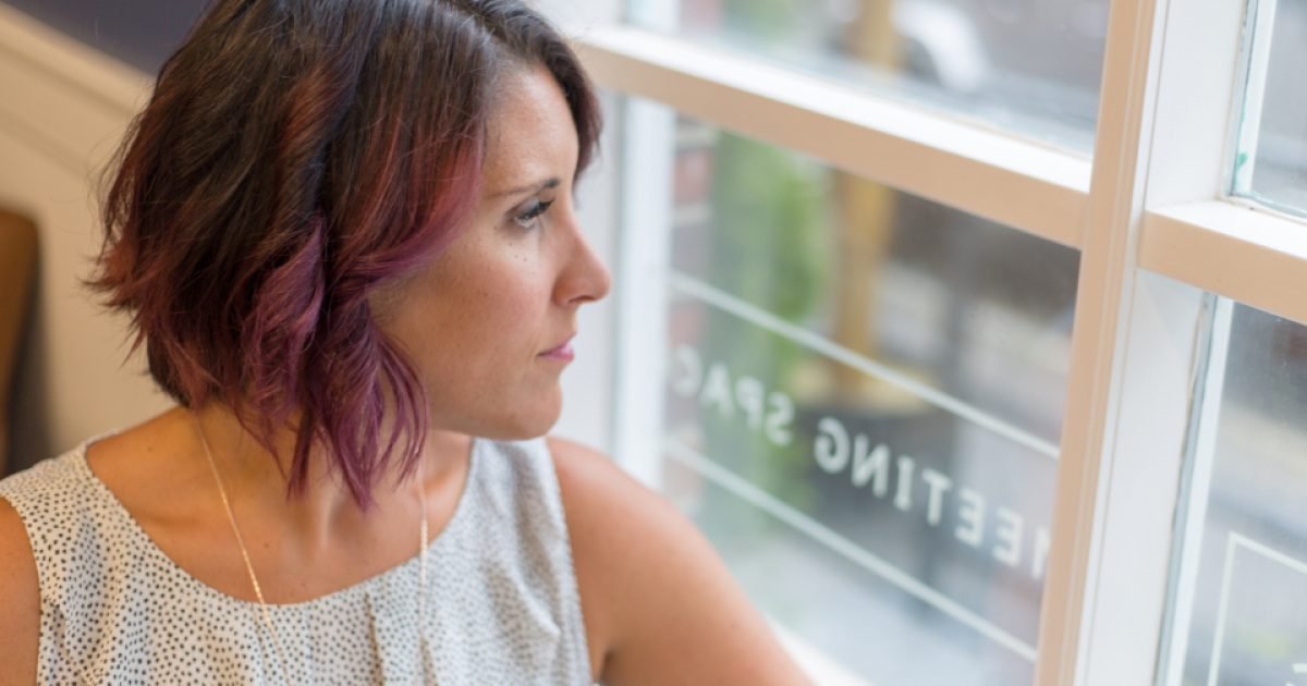 Woman sitting by a window looking outside with a thoughtful expression