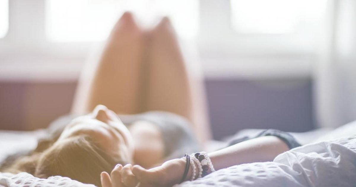 Woman lying on a bed in the morning light with her arms above her head