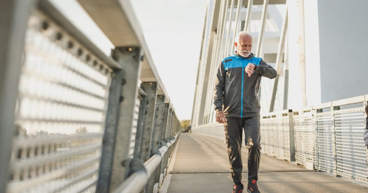 Older man in a tracksuit walking across a bridge and checking his watch