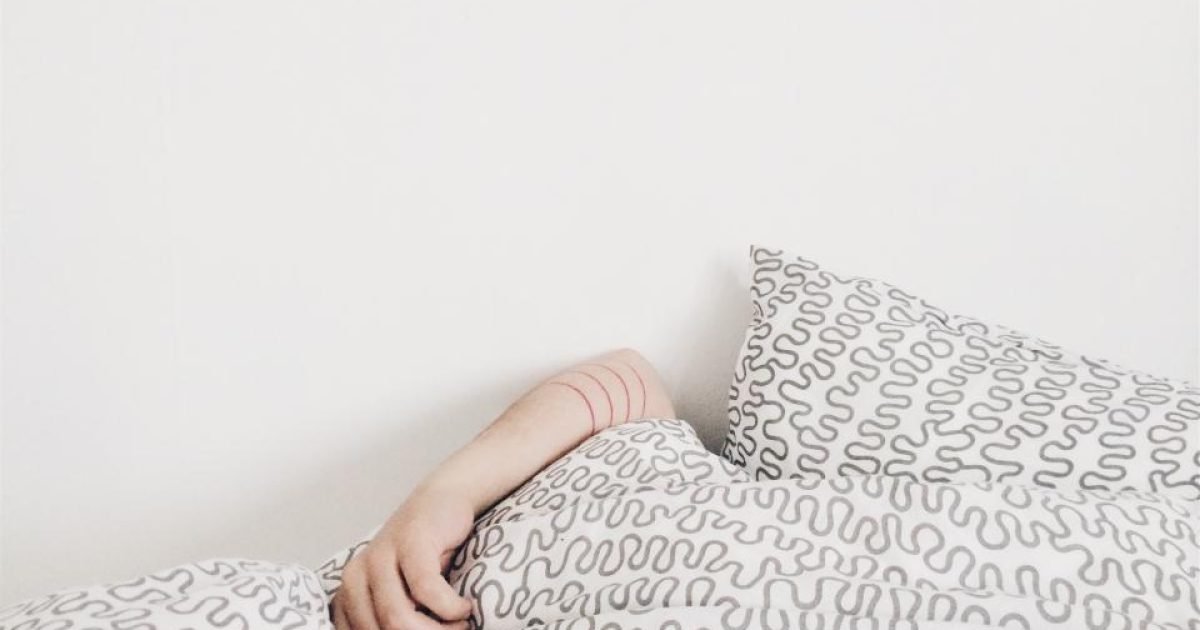 Person lying under a patterned duvet with one arm visible on the bed
